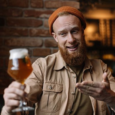 Man holding glass of beer at a distance, smiling at it. Adobe stock